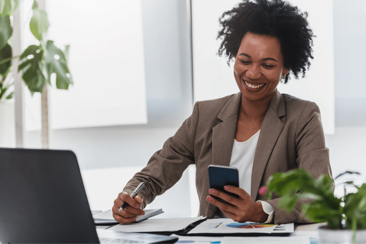 Woman sitting in front of her laptop using her mobile device, Go to Official Release of Simpli.fi Autopilot AI: Revolutionize Your Advertising Workflow Today