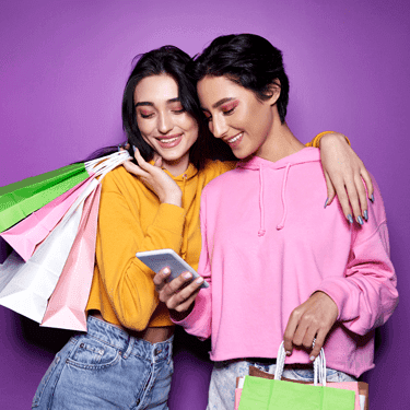 Two girls holding shopping bags looking at a mobile phone